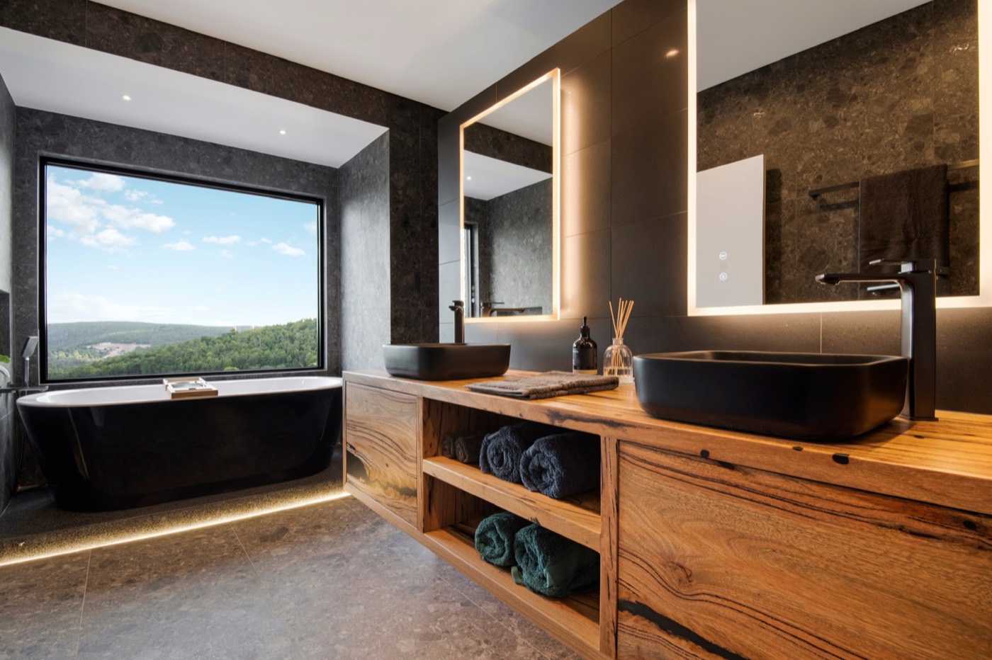Dark stone bathroom with timber vanity and forest outlook