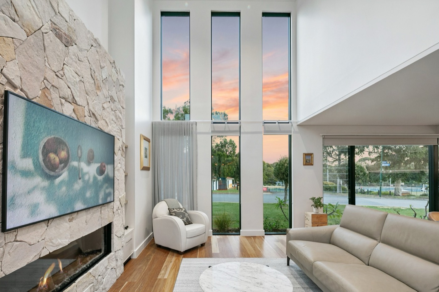 Double-height Morden Street living room with a textured stone fireplace and tall windows