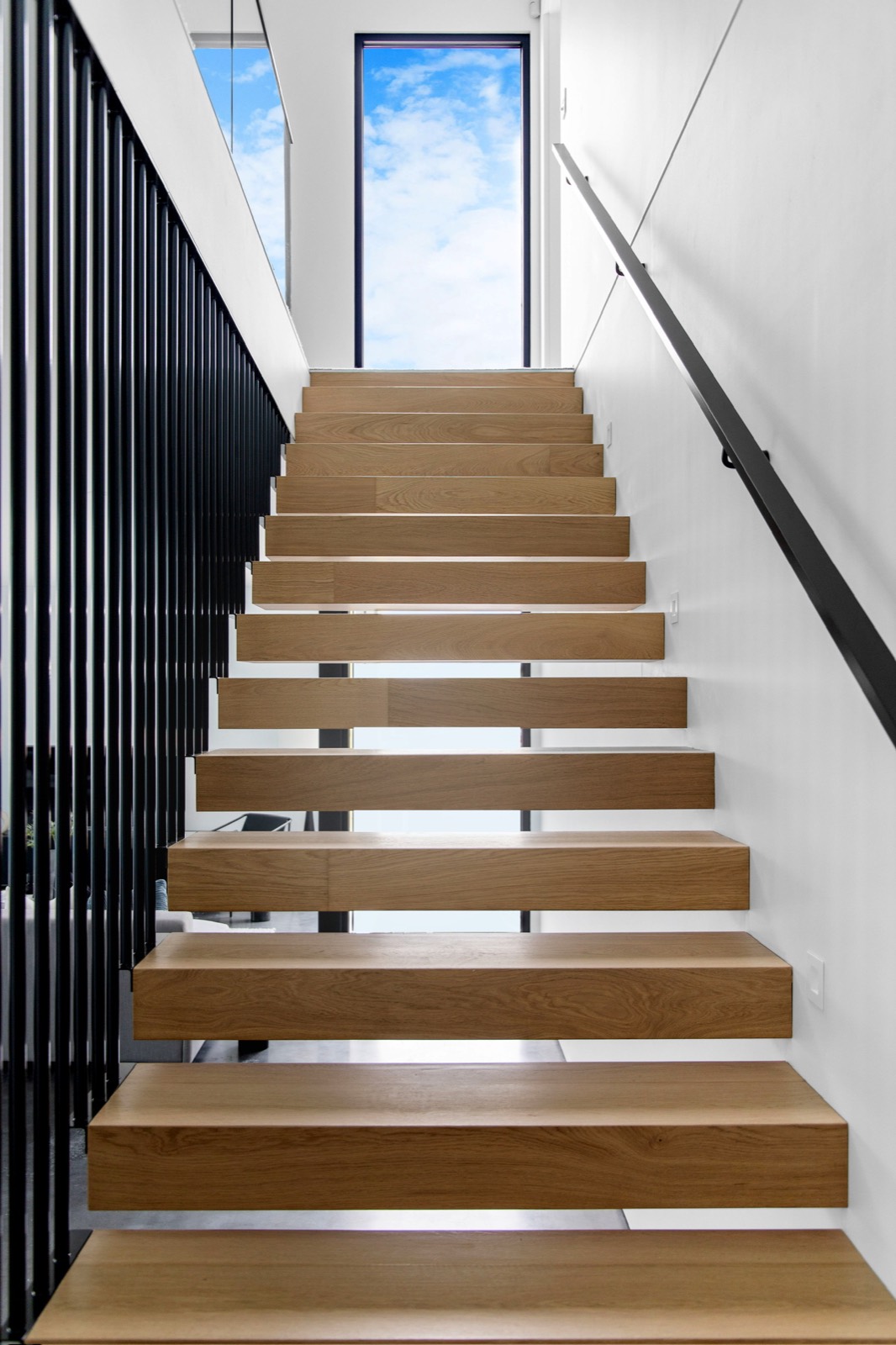 Timber stair ascending toward a tall sky-facing window