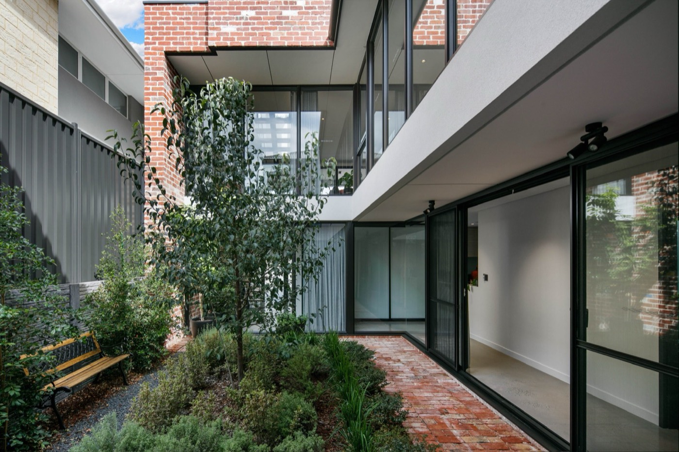 Lush planted courtyard enclosed by brick and black-framed glazing