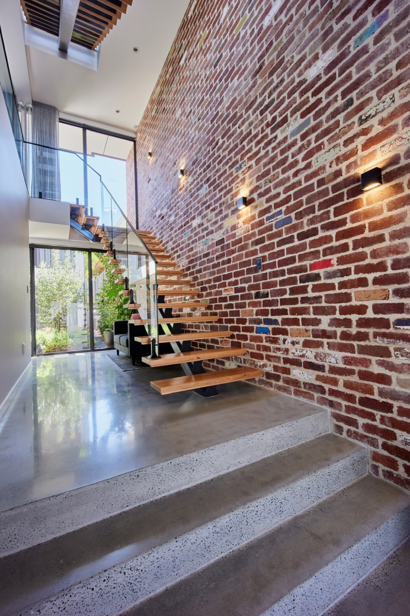 Timber stair rising beside a tall recycled brick wall at Nova Lane
